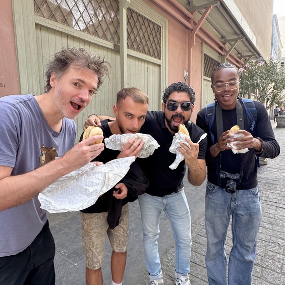 Four people eating sandwiches on a street. 1