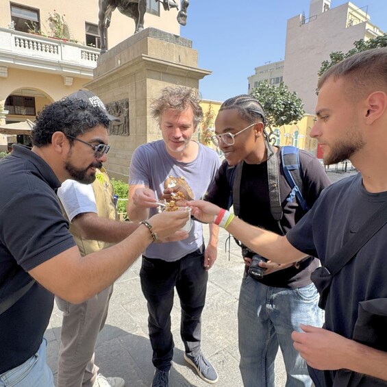 A group of people outdoors, one person holding a food item. 4