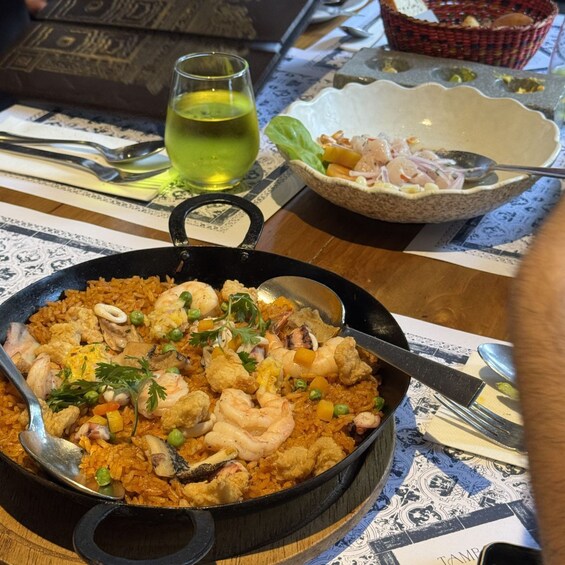 A pan of shrimp and rice dish on a table with a glass of white wine and a bowl of salad. 3