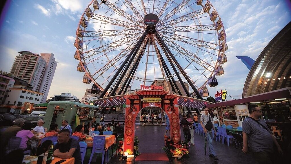 Una ruota panoramica, un arco tradizionale e una strada animata con persone e bancarelle di cibo. 4