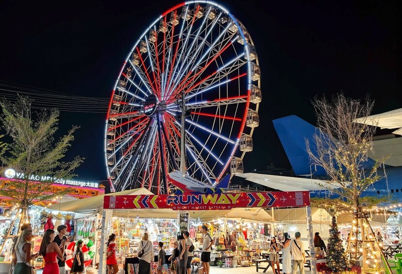 Una grande ruota panoramica con un mercato notturno sottostante, con bancarelle e persone. 2
