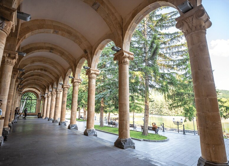 A covered walkway with arches and columns, surrounded by trees and a body of water. 3