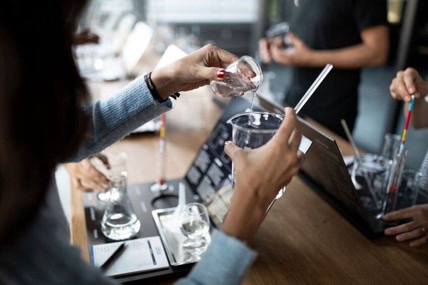 A person pouring a liquid into a glass, with a tablet and other glasses on the table. 2