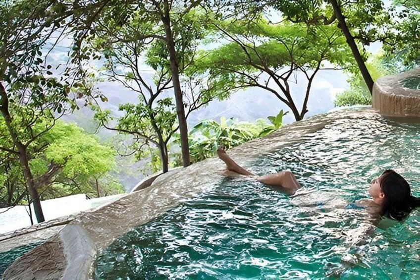 A person relaxing in a pool with a view of trees and a rocky landscape. 1
