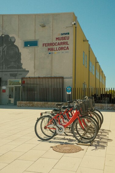 A red bicycle parked in front of a building with a mural and a sign that reads 'Museu Ferrocarril Mallorca'. 5