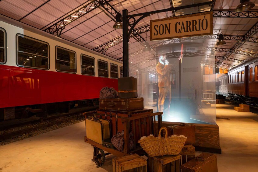 A vintage train station with a red train, luggage carts, and a sign that reads 'SON CARRIÓ.' 1