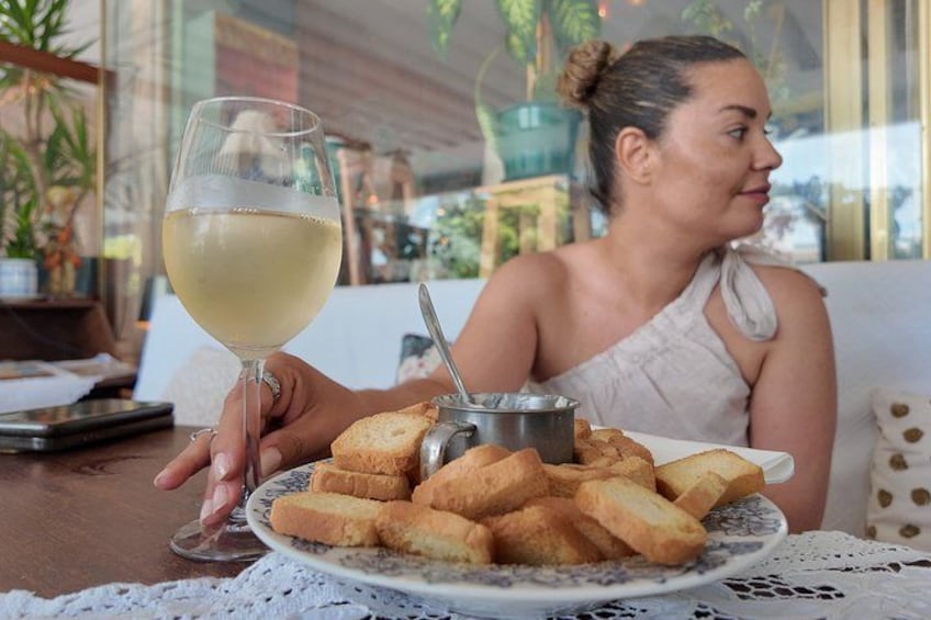 A person holding a glass of white wine and a plate of bread. 3