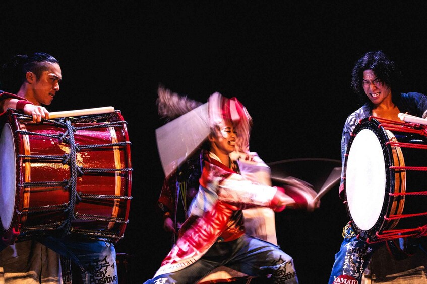Three individuals playing large drums. 3