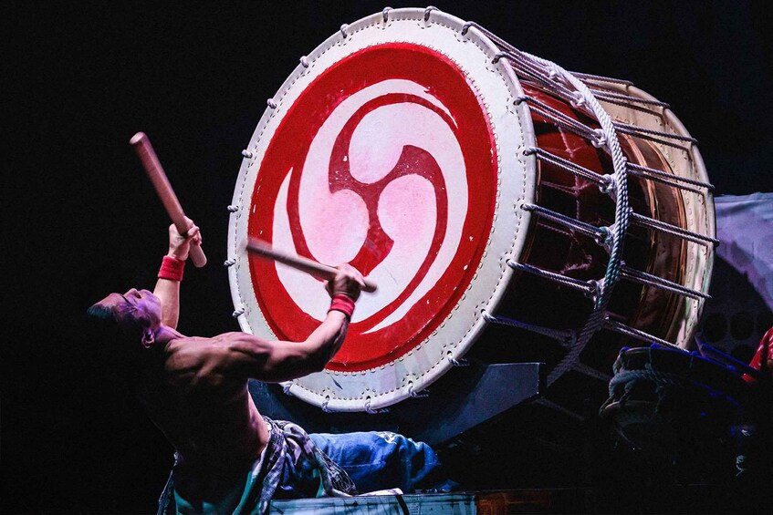 A person playing a large drum with a red and white design. 5