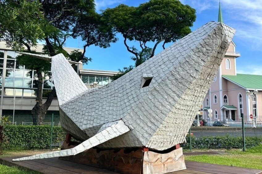 A large, textured sculpture resembling a fish in a park with a building in the background. 3