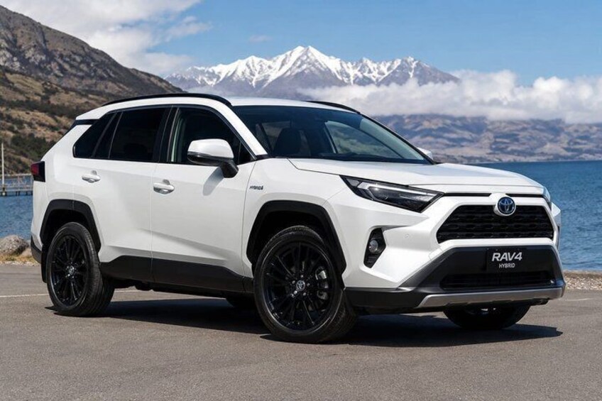 A white Toyota RAV4 Hybrid SUV parked on a road with a mountainous landscape in the background. 3