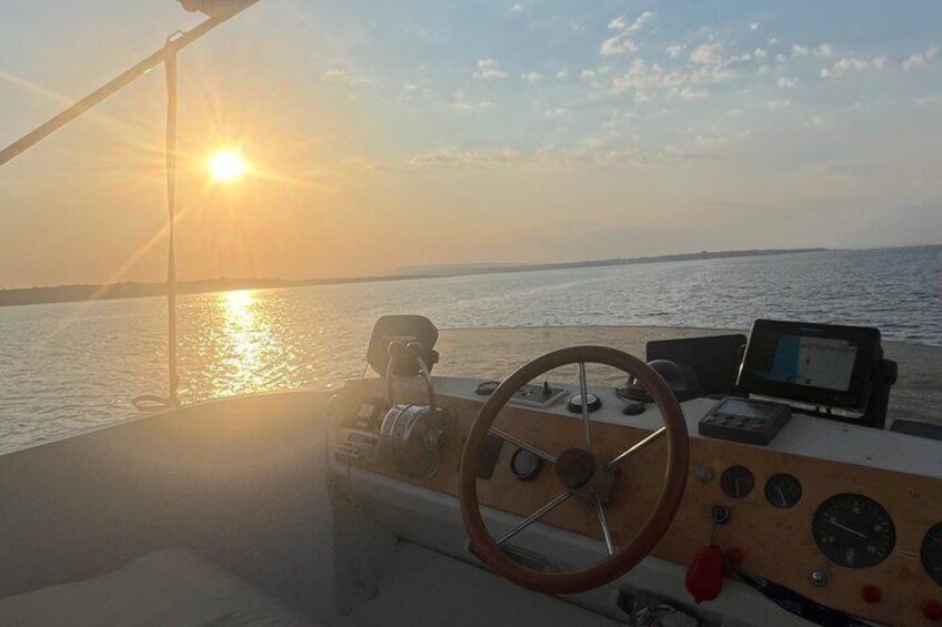A boat's steering wheel, control panel, and a sunset over the water. 2