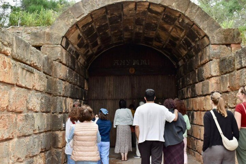 A group of people standing in front of an arched stone structure with inscriptions. 3