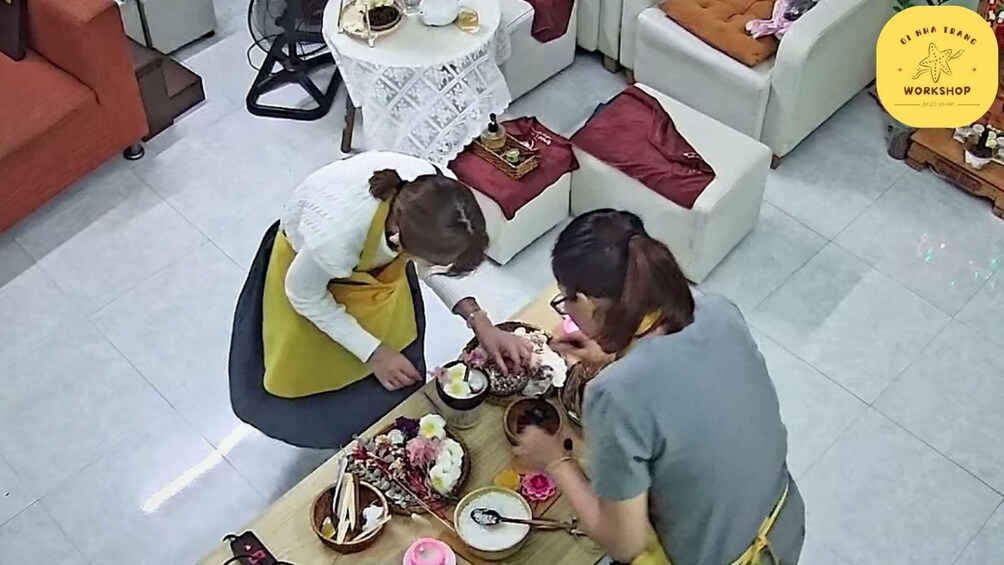 Two people sitting at a table with food and drink, in a room with a white couch and a small round table. 4