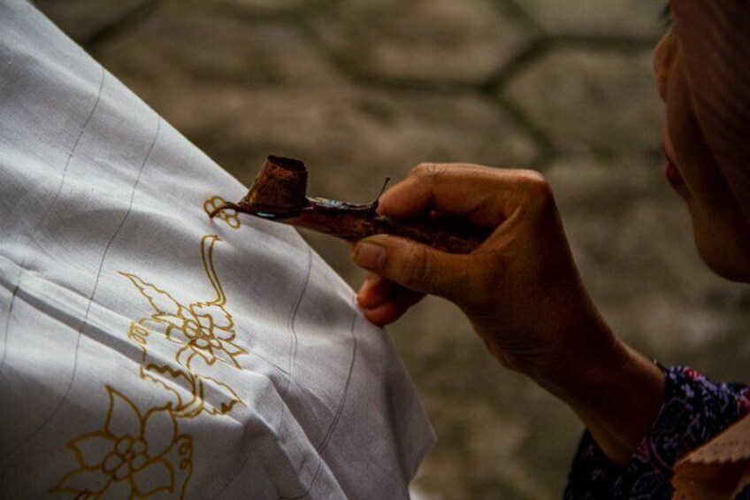 A person sewing a golden embroidery on a white fabric. 4