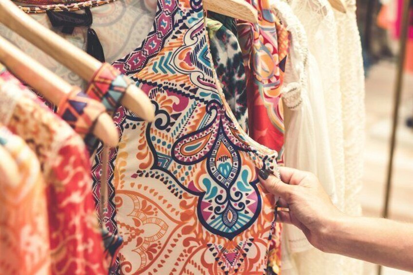 A person examining colorful patterned fabric on a clothing rack. 2