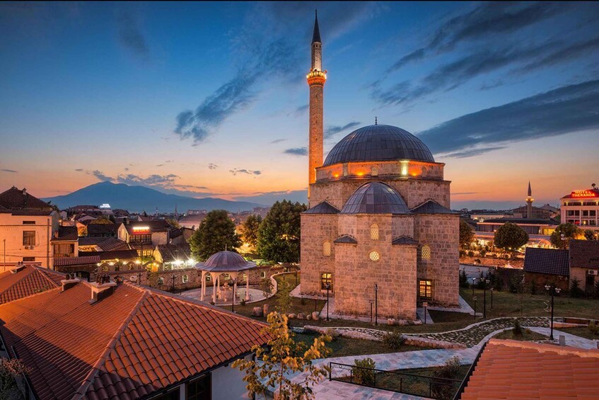 A mosque with a tall minaret and a dome, surrounded by buildings and a mountain in the background. 4