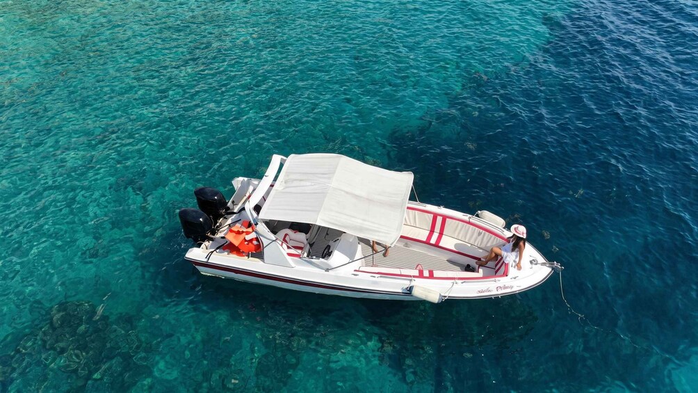 A small motorboat with a canopy, anchored in clear turquoise water. 1