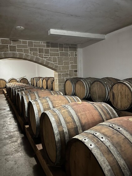 Wooden wine barrels stacked in a warehouse with stone walls and a concrete ceiling. 2