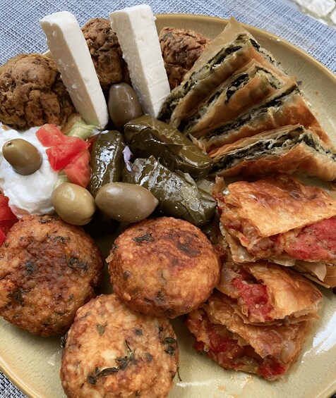 Une assiette contenant divers aliments, notamment des feuilles de vigne farcies, des olives, des tomates et des galettes de viande. 4