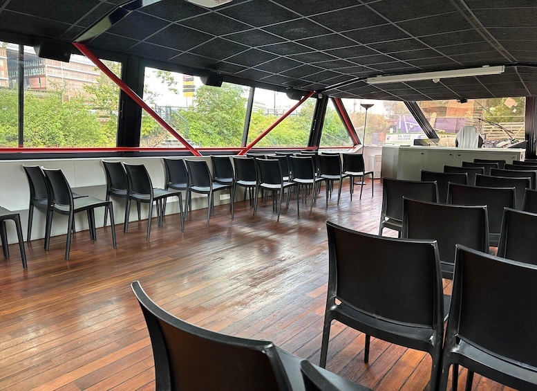 An indoor space with rows of black chairs, wooden flooring, and large windows with red structural supports. 3