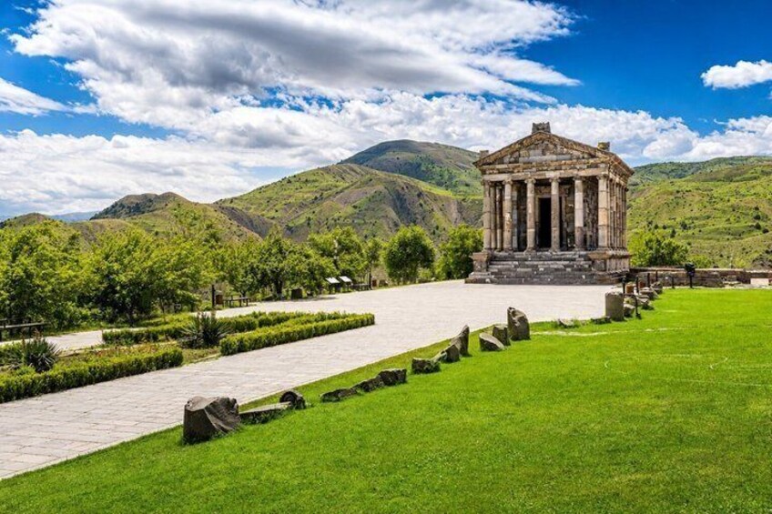 A classical temple with columns, surrounded by a well-maintained lawn and pathways, set against a backdrop of rolling hills. 4