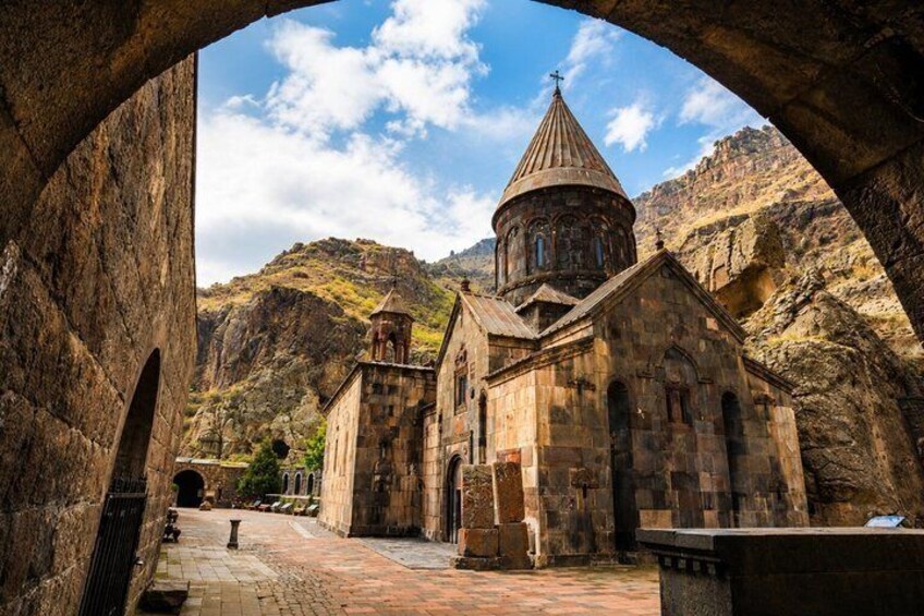 A stone church with a dome and bell tower, set against a mountainous backdrop. 5