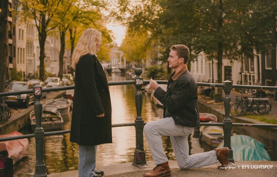 A man proposing to a woman on a bridge with a canal in the background. 1