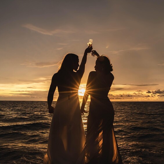 Two people toasting with a glass of champagne at sunset by the ocean. 3