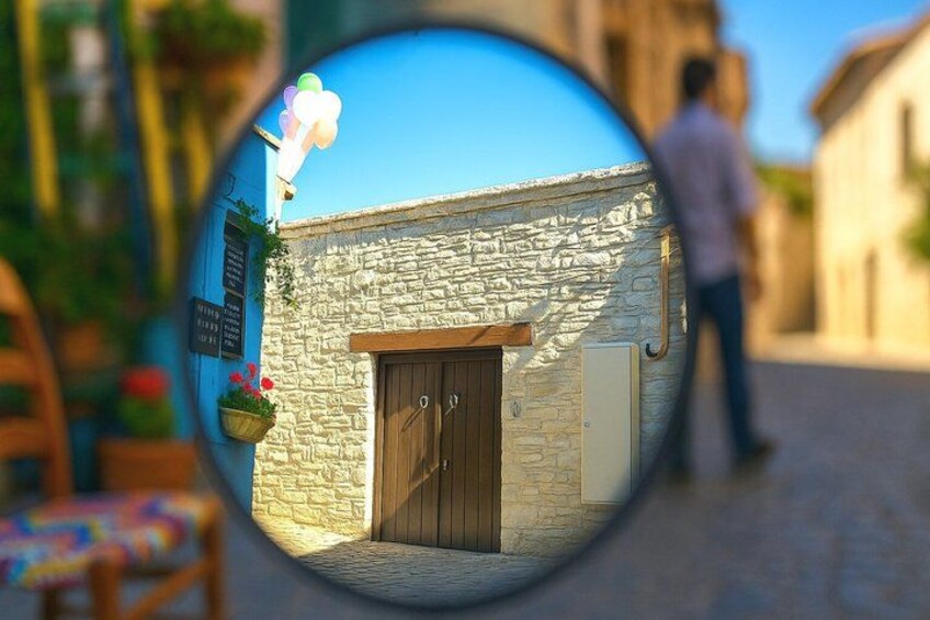 A stone building with a wooden door, a person walking in the background, and a circular mirror reflecting the scene. 3