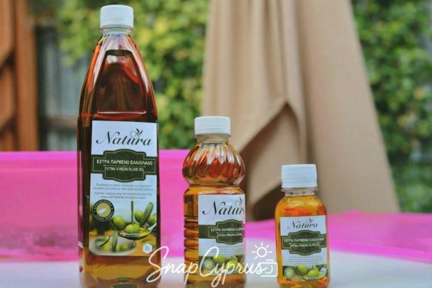 Three bottles of extra virgin olive oil with labels, placed on a pink surface outdoors. 4
