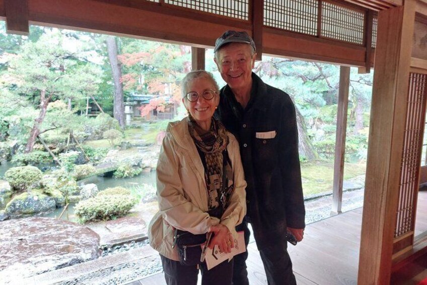Two people standing in a traditional Japanese building with a view of a garden. 1
