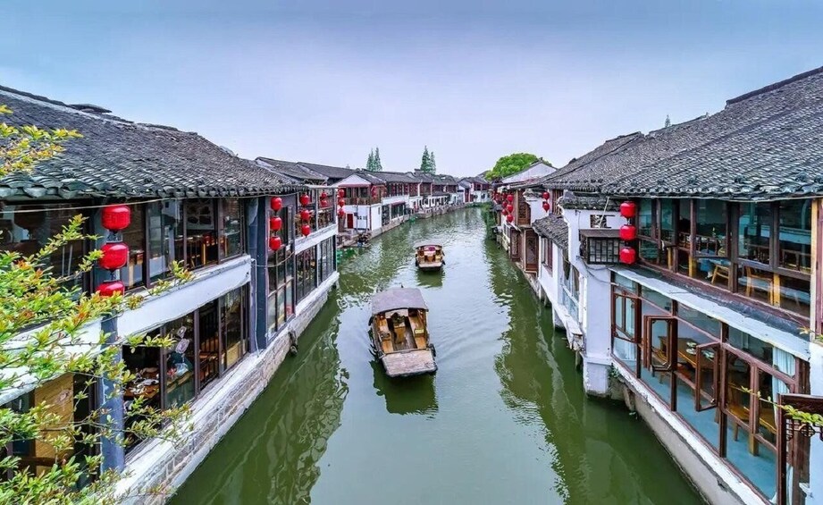 A narrow waterway flanked by traditional buildings with red lanterns, a boat in the center, and a clear sky. 2