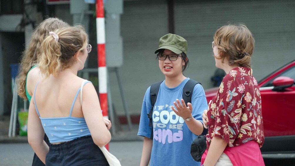 Three people conversing on a street with a red car and a traffic light in the background. 4