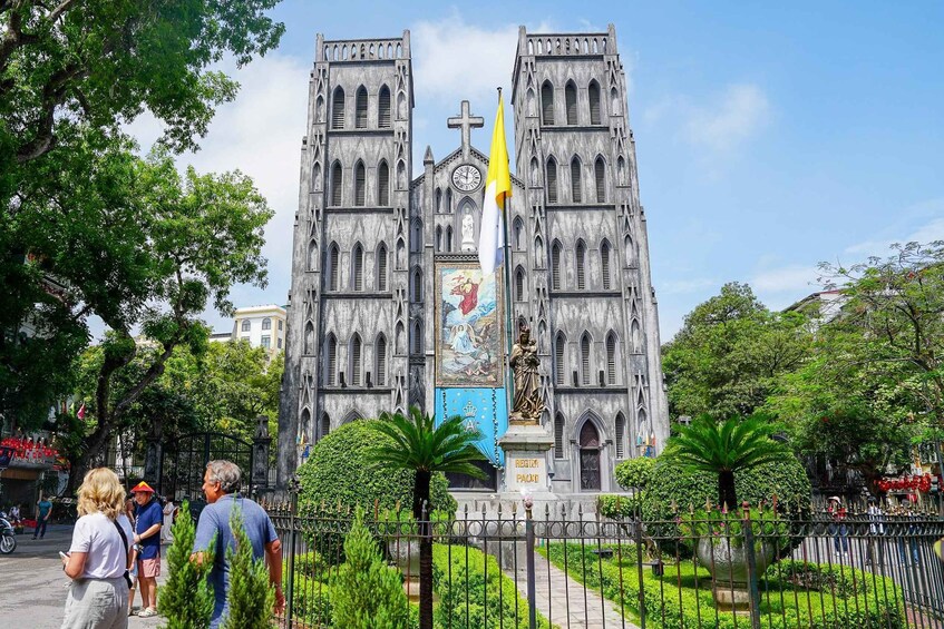 A historic church with twin towers and a central cross, surrounded by lush greenery and a statue. 5