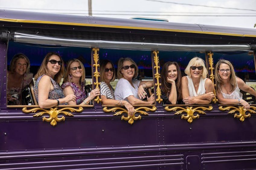 A group of people seated in a purple train carriage with ornate golden handles. 4