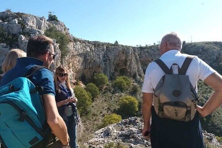 Three people standing on a rocky outcrop with a mountainous landscape in the background. 3