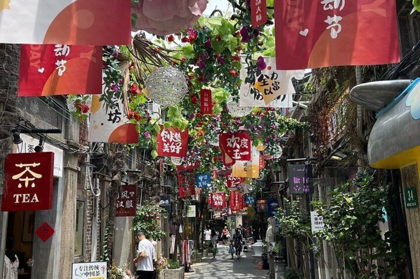A narrow street with hanging decorations, signs, and a tea shop. 4