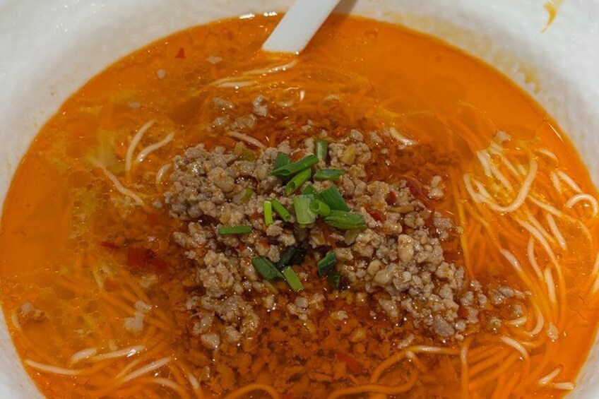 Una ciotola di zuppa di noodles piccante con brodo rosso, guarnita con carne macinata e cipollotti. 5