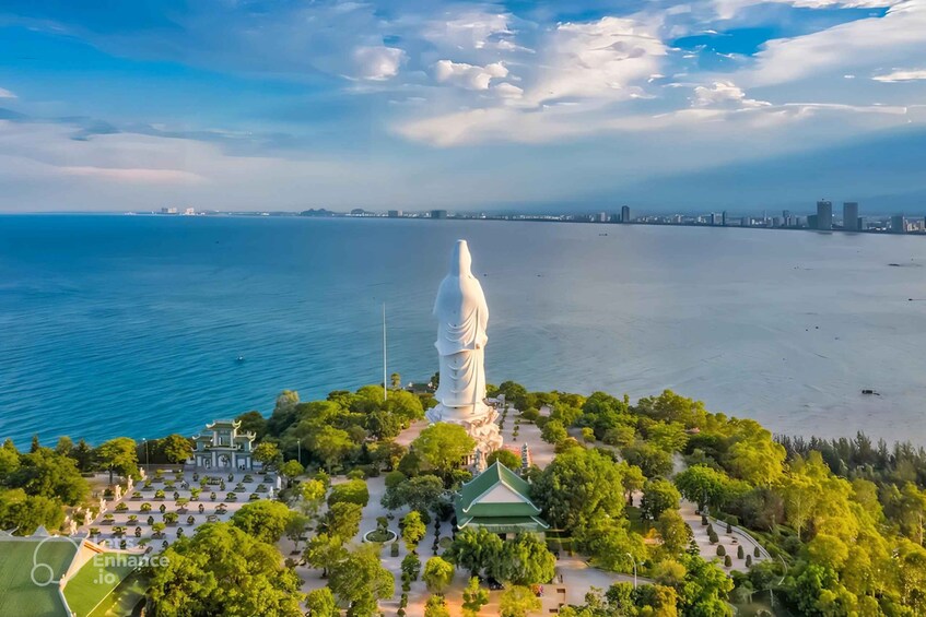 A large white statue surrounded by a park with a body of water in the background. 2