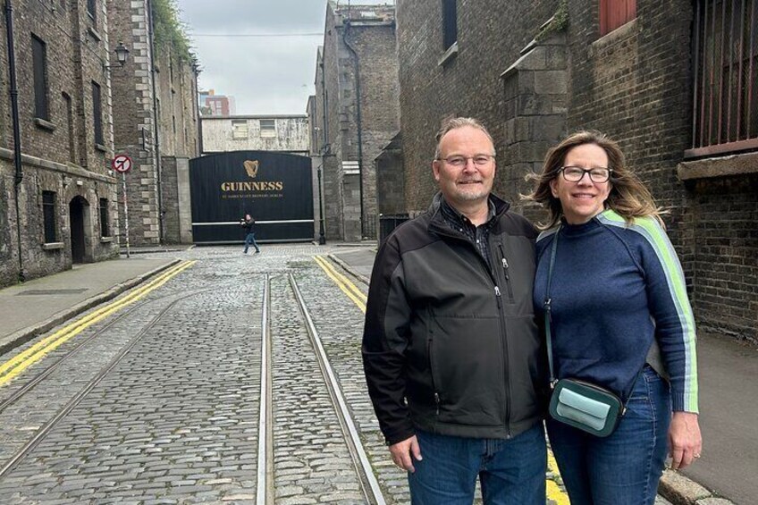 A man and a woman standing on a cobblestone street with a Guinness sign in the background. 4