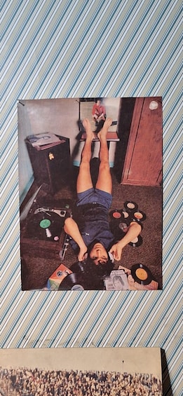 A person lying on the floor surrounded by vinyl records and a guitar. 3