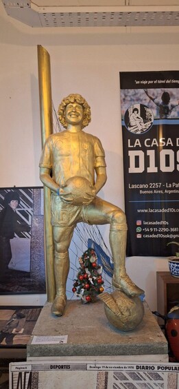 A golden statue of a soccer player holding a ball, with a poster and a small Christmas tree in the background. 5