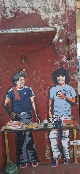 A mural on a weathered red wall with two figures, one holding a drink and the other a radio, and a sign above stating 'valores mas importantes de la vida'. 2