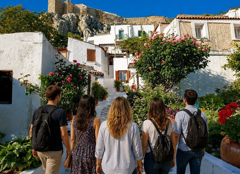 A group of people walking down a narrow street lined with white buildings and blooming flowers. 3