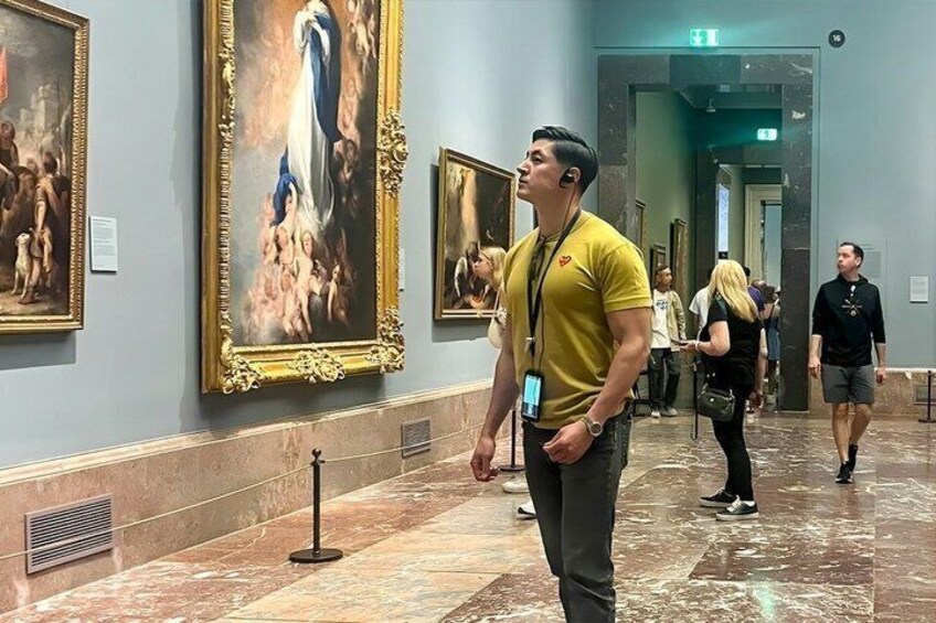A museum corridor with marble floors and framed paintings on the walls. 1