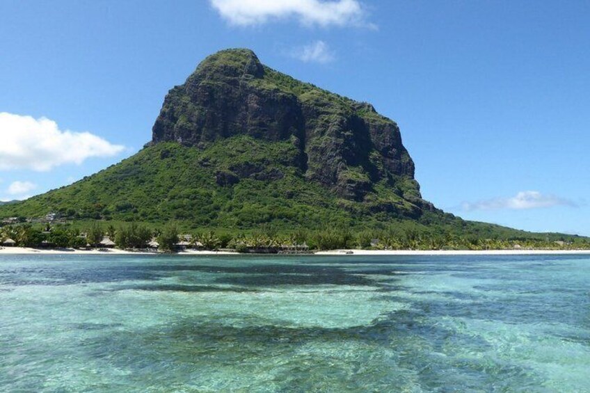 A clear tropical beach with a prominent green mountain in the background. 1