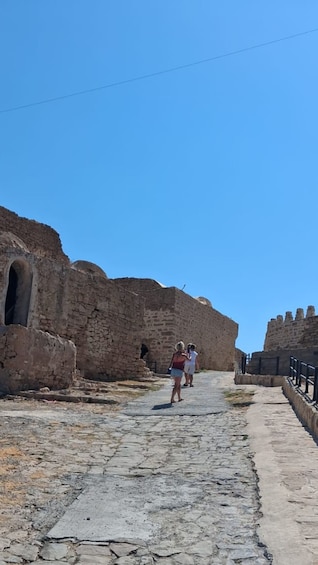 A stone pathway leading through ancient ruins with arched openings and a clear blue sky. 2