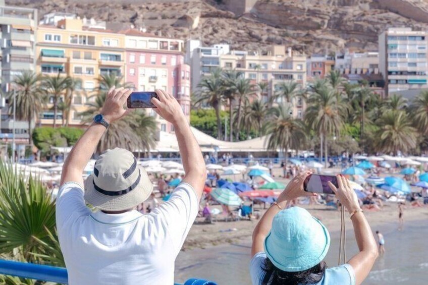 A beach with people taking photos, palm trees, and colorful umbrellas. 5