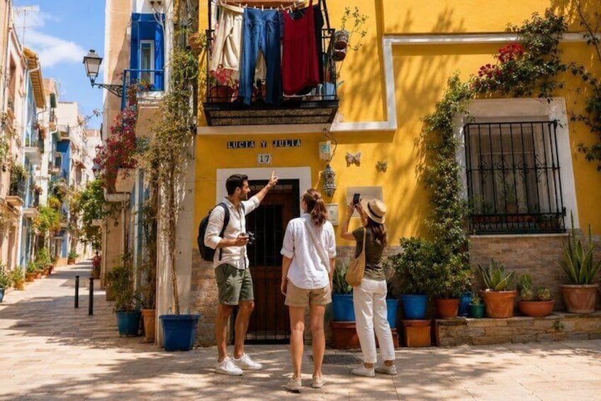 A narrow street with buildings, a person pointing, and a group of people taking photos. 1